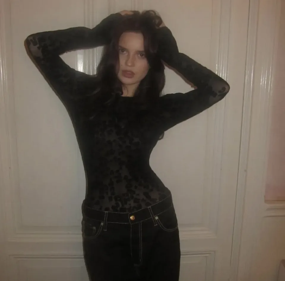 A sheer black top with a flocked leopard pattern, worn with dark denim jeans.