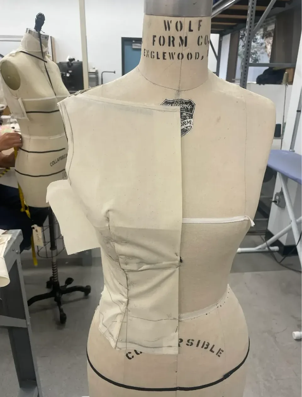 A calico toile pinned on a dress form, seen from the front, with the seams marked in pencil and the raw edges left open.