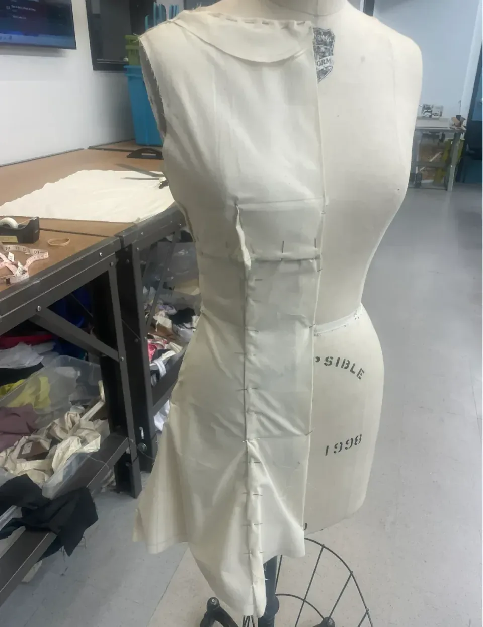 A second calico toile on a dress form, further developed, with a fitted bodice and shaping seams pinned in place.