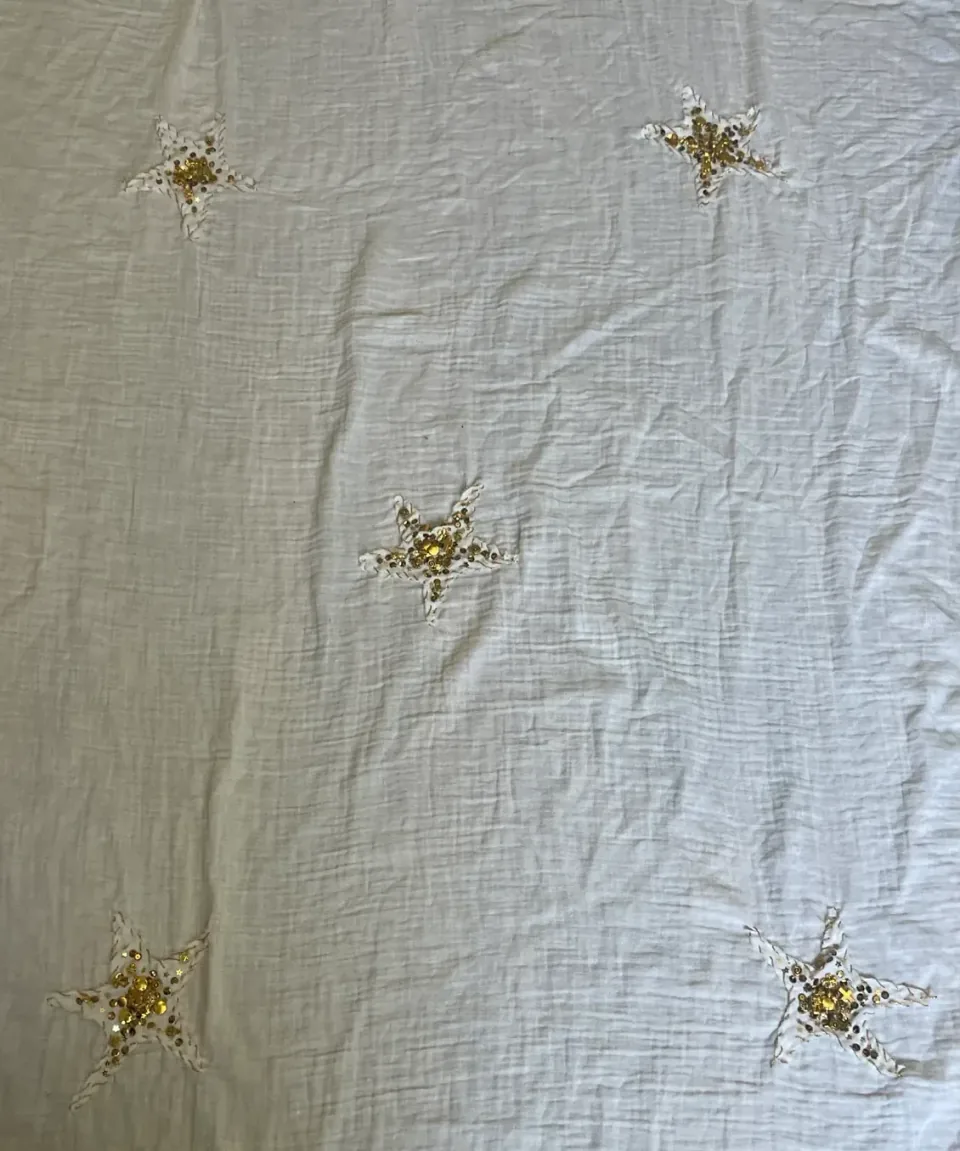 Photograph of a white fabric panel with five embroidered stars spread across it, each with a cluster of sequins and beads at the centre.